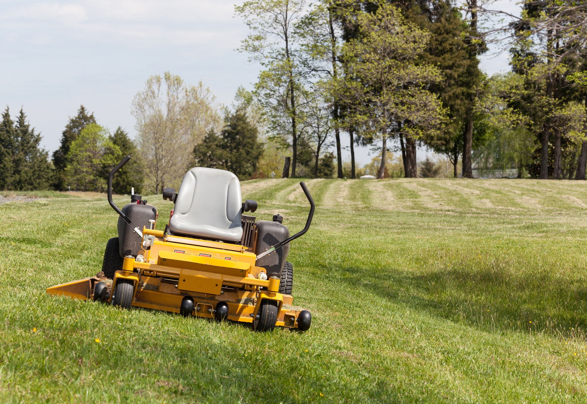 No person on expansive lawn with a yellow zero-turn mower